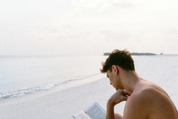 topless man reading book tout en etant assis a la plage